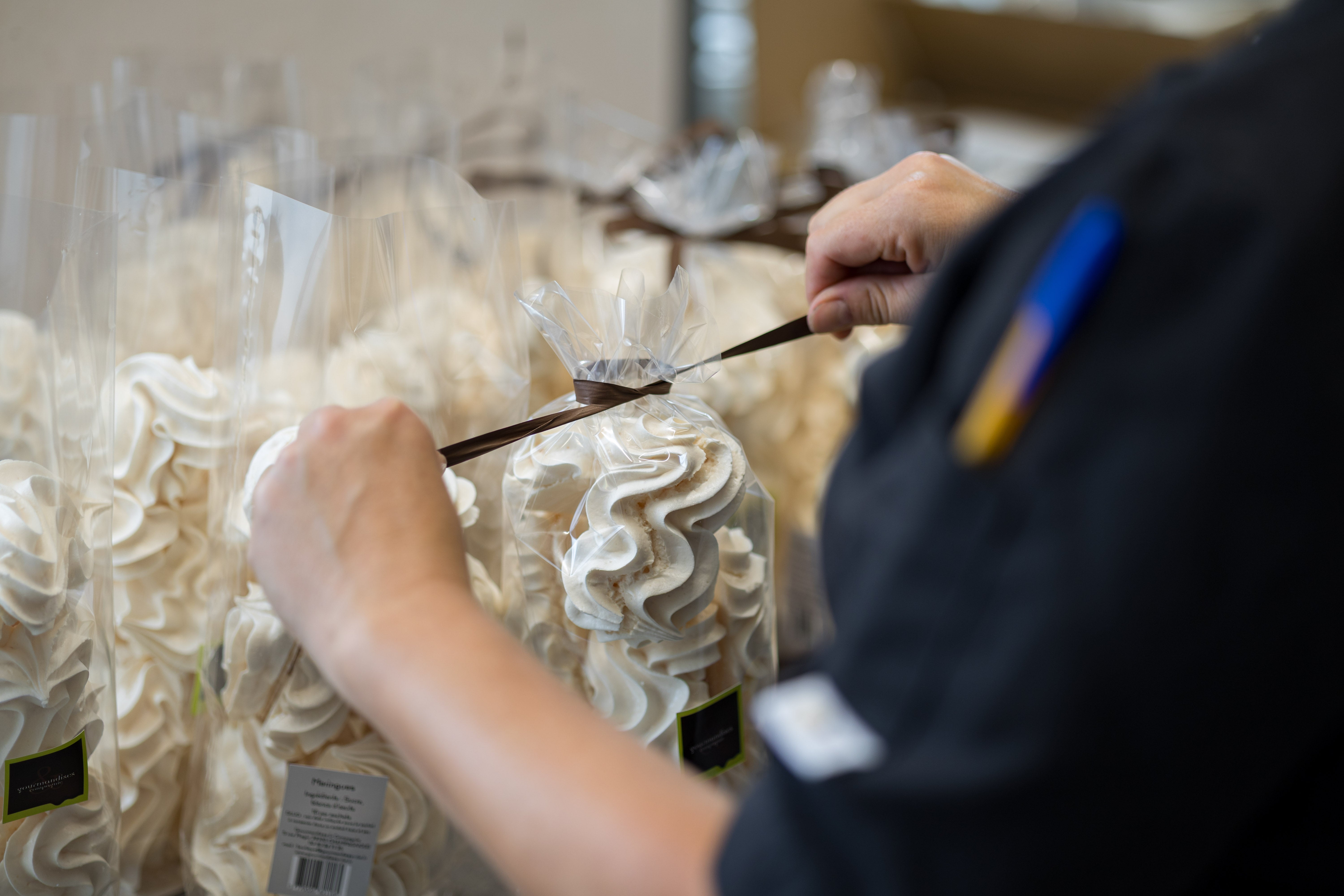 Deux mains nouent un ruban brun sur un sachet de meringues, à l’atelier.