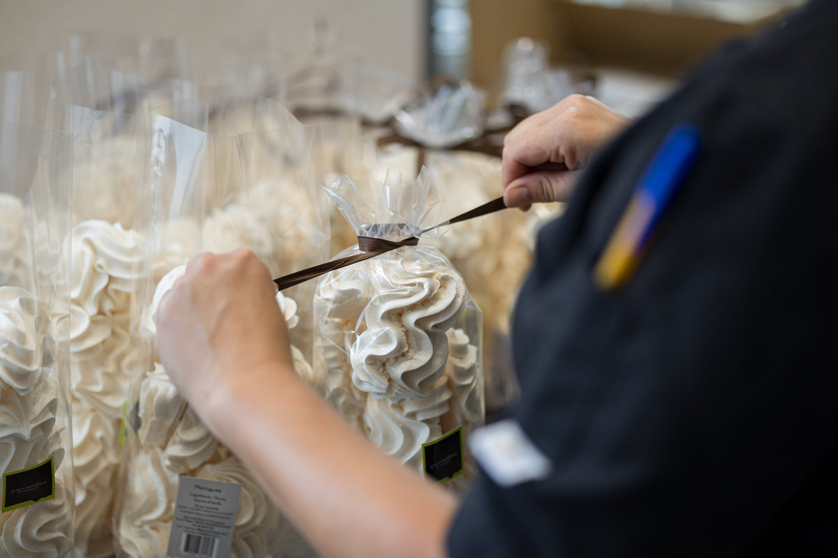 Deux mains nouent un ruban brun sur un sachet de meringues, à l’atelier.