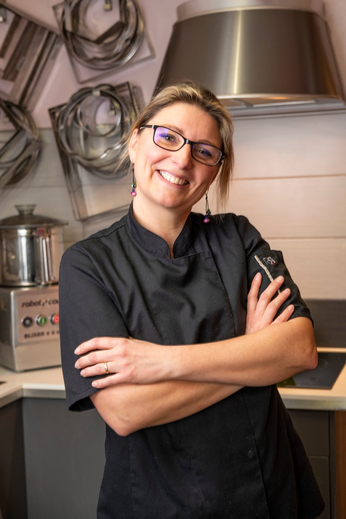 Mélanie Plantard dans son atelier, bras croisés et sourire, en veste de cuisine noire
